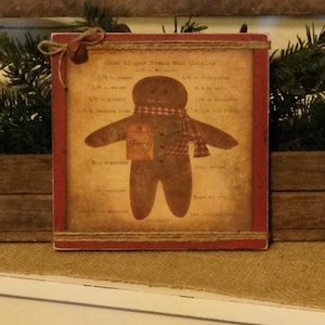 May include: A rustic, framed sign featuring a gingerbread man illustration. The sign has a red border and a twine accent. The gingerbread man wears a plaid scarf and holds a tag that says "Joy". The sign also includes a recipe for "Olde Ginger Bread Man Cookies".