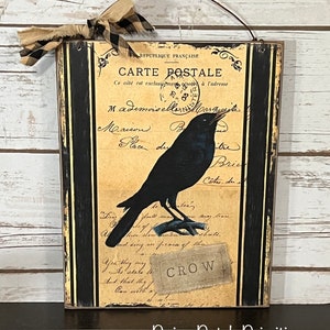 May include: A vintage-style postcard with a black crow perched on a branch. The postcard is decorated with black and white stripes and has the text "CARTE POSTALE" and "CROW" on it.