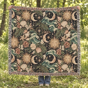 Peut inclure: Un plaid tissé présentant un fond sombre avec un motif répétitif de soleils, de croissants de lune, d'étoiles, de coquillages, d'étoiles de mer, de feuilles de palmier tropicales et de fleurs d'hibiscus dans des tons or, sarcelle et crème avec des bords à franges.