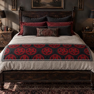 May include: A bed runner featuring a repeating pattern of red pentagrams on a dark gray background, placed across a light beige bedspread. The runner has a thin gray border and is positioned over a collection of dark gray and deep red pillows.