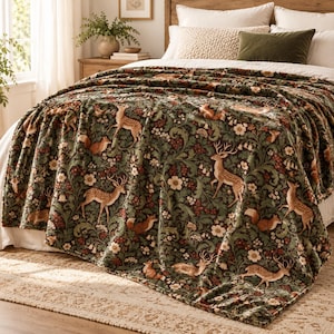 May include: A dark green plush throw blanket featuring a repeating pattern of deer, foxes, and white flowers with red berries. The blanket is draped over a bed with white bedding, a textured cream pillow, and a solid olive green pillow.