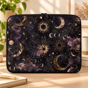 May include: A rectangular laptop sleeve featuring a dark purple and black celestial print with gold-toned illustrations of suns, various moon phases, and scattered stars. The case has a black zipper closure along the top edge.