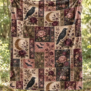 Peut inclure: Une couverture rectangulaire présentant un motif patchwork composé de fleurs sombres, de corbeaux noirs, de croissants de lune et de petites chauves-souris. La palette de couleurs comprend des tons bordeaux, vert sourd, crème et noir.