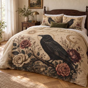 May include: A beige duvet cover and two matching pillowcases featuring a large black raven perched on a branch, surrounded by detailed illustrations of dark red and white roses, a golden sun, and a crescent moon on a light tan background.