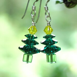 May include: A pair of silver dangle earrings featuring a green and yellow crystal Christmas tree design.