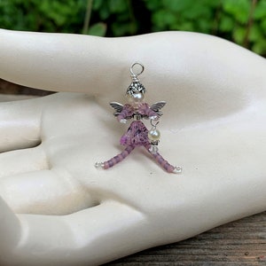May include: A purple beaded fairy charm with silver wings and a pearl accent. The fairy is holding a small pearl charm.