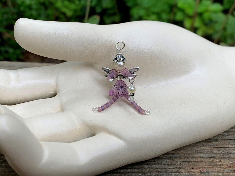 May include: A purple beaded fairy charm with silver wings and a pearl accent. The fairy is holding a small pearl charm.