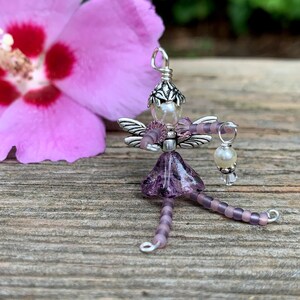 May include: A purple beaded fairy charm with silver wings and a pearl accent. The fairy is holding a small pearl and crystal charm.