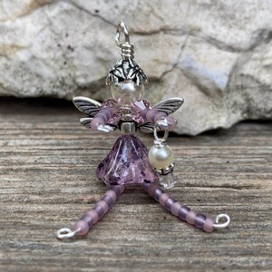 May include: A purple beaded fairy charm with silver wings and a pearl hanging from her hand.
