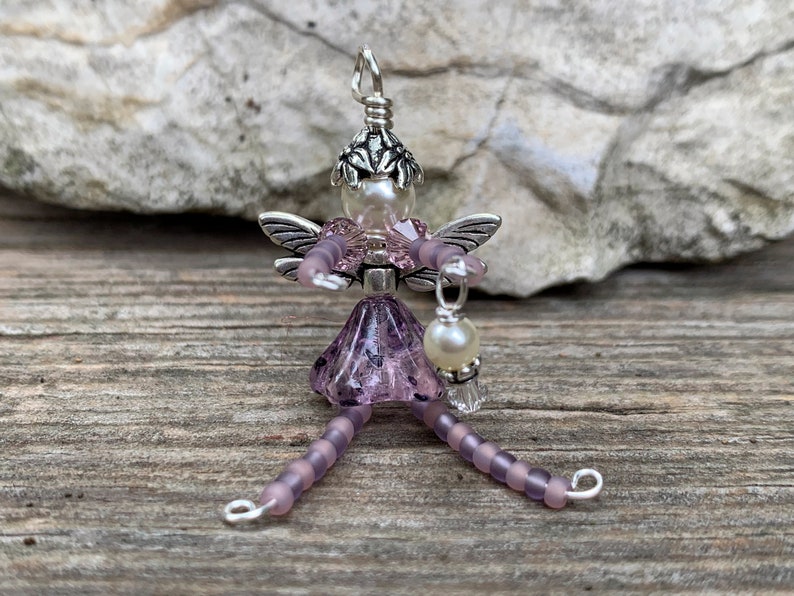 May include: A purple beaded fairy charm with silver wings and a pearl hanging from her hand.