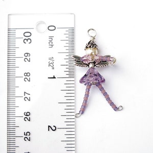 May include: A purple beaded fairy charm with silver wings and a pearl bead. The charm is approximately 1 inch in length.