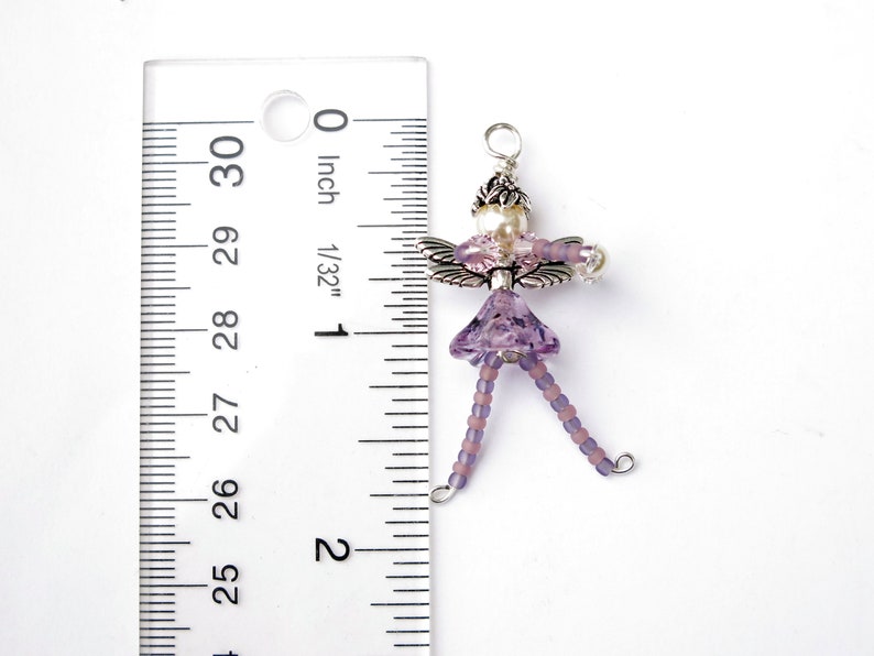 May include: A purple beaded fairy charm with silver wings and a pearl bead. The charm is approximately 1 inch in length.