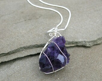 May include: A silver chain necklace with a purple amethyst crystal pendant. The crystal is wrapped in silver wire.