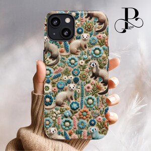 May include: A phone case with a floral pattern featuring embroidered ferrets in shades of brown, white, and gray. The background is a cream color with blue, pink, and orange flowers.