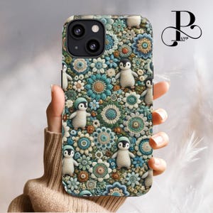 May include: A phone case with a colorful floral pattern featuring crocheted flowers and penguins. The case is made of a hard plastic material and has a cutout for the camera lens.