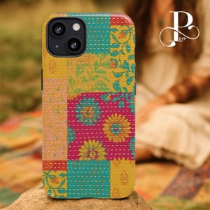 Puede incluir: Funda de teléfono de patchwork colorida con diseño floral. Presenta cuadrados de tela amarillos, rosas y turquesas, cosidos con hilo blanco. Diseñada para un smartphone con cámara de doble lente.
