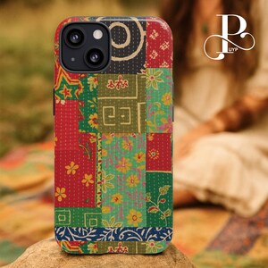 May include: A colorful patchwork phone case featuring a variety of floral and geometric patterns in red, green, yellow, and blue. The case has a black camera module and a textured, quilted appearance, giving it a unique, handcrafted look.
