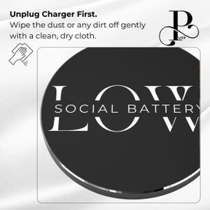 May include: A black round phone charger with the text "LOW SOCIAL BATTERY" in white lettering. The charger is on a white surface.