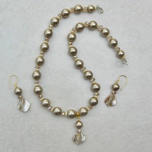 May include: A pearl necklace with a shell pendant and matching earrings. The necklace is made of beige pearls and has a gold clasp. The earrings are also made of beige pearls and have gold hooks.
