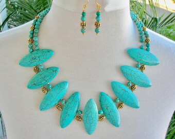 May include: A turquoise necklace and matching earrings set. The necklace features large, oval turquoise stones interspersed with gold-colored beads. The earrings have a similar design, with turquoise beads and gold accents. The jewelry is displayed on a white mannequin.