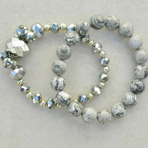 May include: Two bracelets, one with silver and gold beads and the other with gray and white marbled beads.