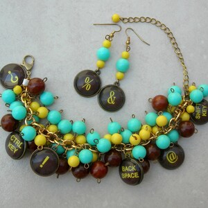 May include: A turquoise and yellow beaded necklace with a gold chain and brown beads. The necklace features charms with symbols like the percent sign, ampersand, and the words "Shift Key", "Ctrl Key", "Back Space", and "@".