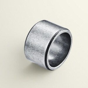 Könnte beinhalten: Ein silberfarbener Ring mit zylindrischem Design. Der Ring hat eine strukturierte Oberfläche und ein breites Band. Das Metall hat ein leicht gealtertes Aussehen mit Variationen in der Silberfarbe. Der Ring ist ein schlichtes, aber auffälliges Schmuckstück.