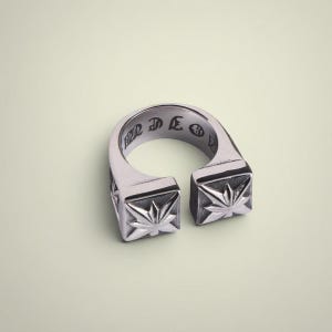 Puede incluir: Anillo plateado con un diseño abierto. Cada extremo del anillo tiene forma cuadrada con un diseño de estrella. El interior del anillo tiene texto grabado. Una joya contemporánea.