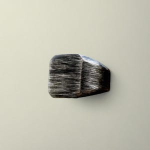 May include: A dark, rectangular cabinet knob with a textured, brushed metal appearance. The knob has a faceted design on one side and a rounded, smooth edge on the other. The color is primarily black and silver.