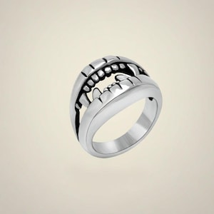 May include: A silver-colored ring with a detailed design of open jaws, featuring rows of teeth. The ring has a smooth, polished finish and a bold, edgy aesthetic. The design is a unique statement piece.