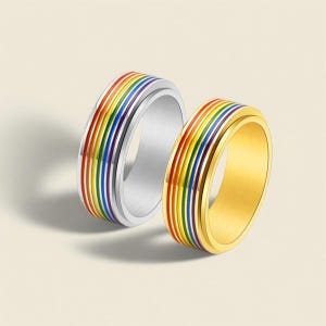 Op de afbeelding: Twee ringen met een regenboogontwerp. Eén ring is zilverkleurig, de andere goudkleurig. De ringen hebben een band met regenboogkleuren: rood, oranje, geel, groen, blauw en paars. De ringen zijn waarschijnlijk van metaal.