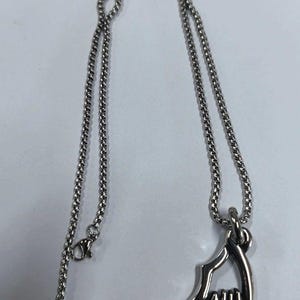 May include: A silver-colored necklace with a pendant shaped like a stylized wing. The chain is a fine, linked design, and the pendant has a detailed, layered appearance. The necklace is displayed on a white surface.