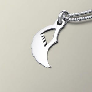 May include: A silver-colored pendant necklace featuring a stylized claw design. The pendant is attached to a delicate chain. The claw shape has a curved edge with several small, parallel lines, creating a textured effect. The necklace is displayed against a neutral background.