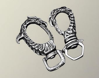 May include: Two silver-colored carabiner clips with dragon-inspired designs. One clip features a dragon head, while the other has a serpent-like design. Both have a sturdy, detailed appearance, suitable for keychains or accessories.