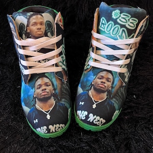 May include: Pair of high-top sneakers featuring a portrait of a person on a blue and green background. The sneakers have white laces and a green sole. The text "#88 BOOM" is visible on the side of one sneaker, and "THE NEST" is on the toe.