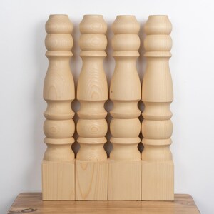 May include: Four unfinished wooden table legs. Each leg is light-colored, with a turned design featuring rounded sections and a square base. The legs are approximately 24 inches tall.