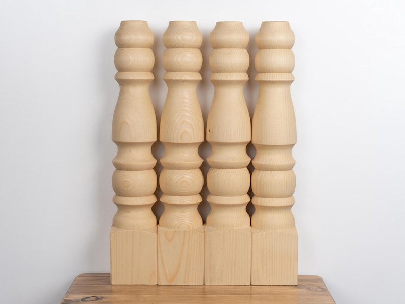 May include: Four unfinished wooden table legs. Each leg is light-colored, with a turned design featuring rounded sections and a square base. The legs are approximately 24 inches tall.