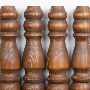 May include: Four wooden furniture legs with a warm brown finish. Each leg features a turned design with rounded sections and a flared base. The wood grain is visible, adding texture and detail to the pieces.
