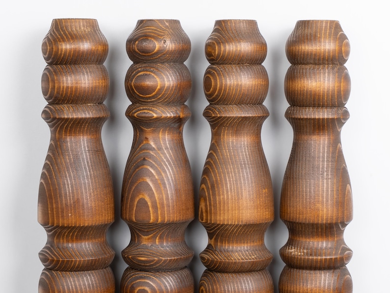 May include: Four wooden furniture legs with a warm brown finish. Each leg features a turned design with rounded sections and a flared base. The wood grain is visible, adding texture and detail to the pieces.