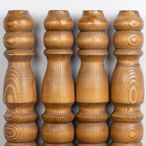 May include: Four wooden furniture legs with a light brown finish. Each leg has a turned design with rounded sections and visible wood grain. The legs are evenly spaced against a white background, showcasing their detailed craftsmanship.
