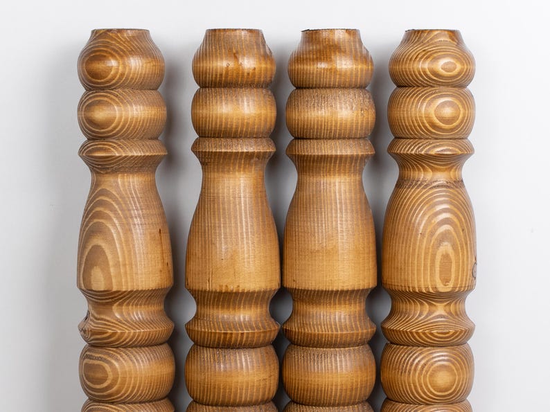 May include: Four wooden furniture legs with a light brown finish. Each leg has a turned design with rounded sections and visible wood grain. The legs are evenly spaced against a white background, showcasing their detailed craftsmanship.
