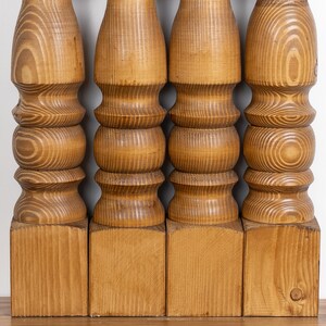 May include: Four wooden table legs, each with a turned, decorative design. The legs are made of light-colored wood, with visible grain patterns. The legs are attached to square bases, and are likely part of a table or other furniture.