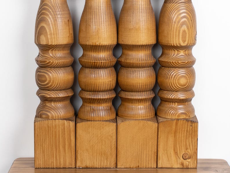 May include: Four wooden table legs, each with a turned, decorative design. The legs are made of light-colored wood, with visible grain patterns. The legs are attached to square bases, and are likely part of a table or other furniture.
