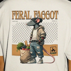 Puede incluir: Camiseta color crema con el texto "FERAL FAGGOT" en una fuente audaz y estilizada. La camiseta presenta un gráfico de una rata con gorro, chaqueta y vaqueros, sosteniendo una bolsa de la compra. El diseño incluye una valla de alambre y un gráfico de llama.