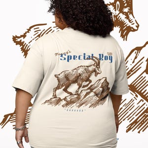 May include: Cream-colored t-shirt with a brown illustration of a mountain goat leaping over rocks. The text "Mommy's Special Boy" is above the goat in blue and brown. The shirt has short sleeves.