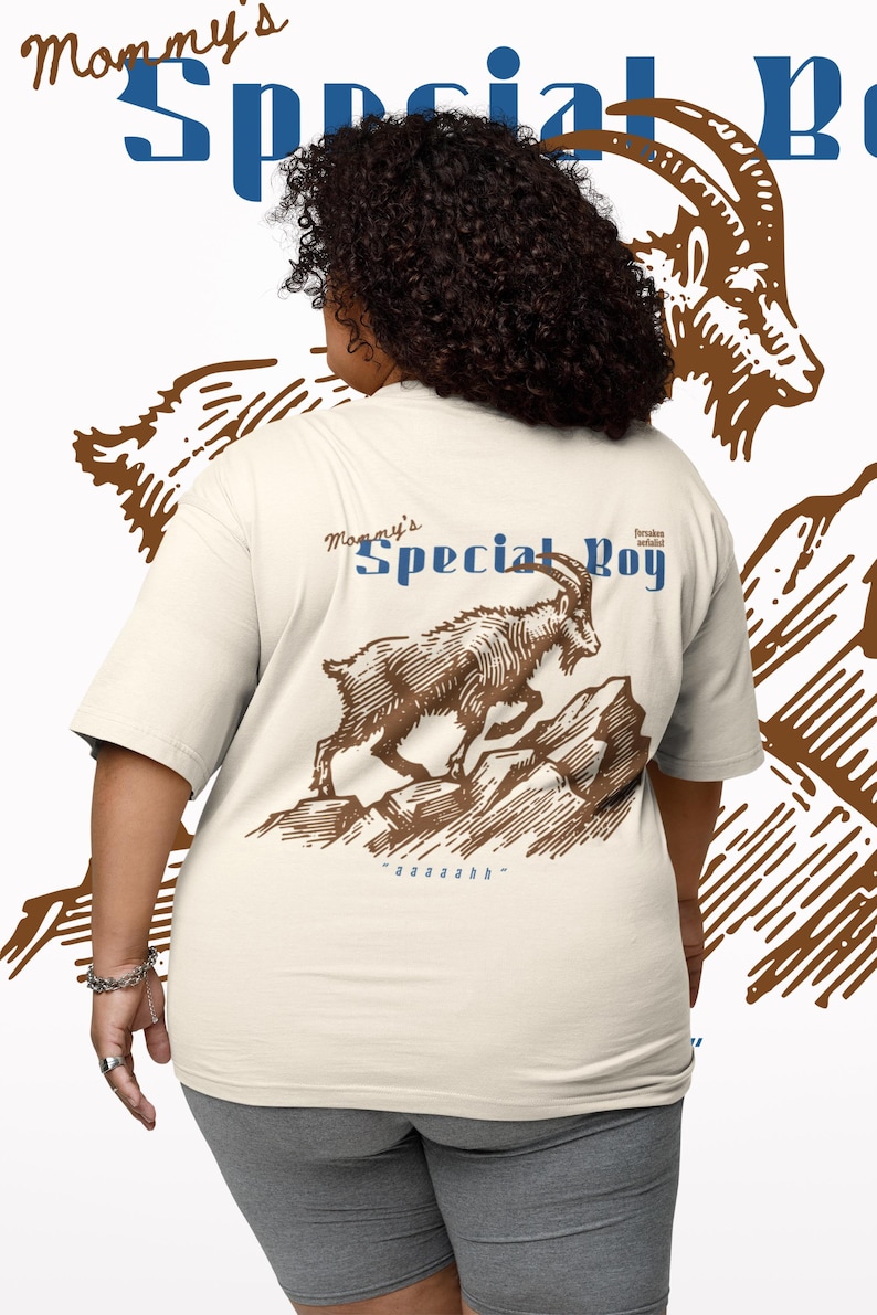 May include: Cream-colored t-shirt with a brown illustration of a mountain goat leaping over rocks. The text "Mommy's Special Boy" is above the goat in blue and brown. The shirt has short sleeves.