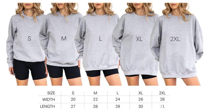 May include: Five women wearing gray sweatshirts in sizes S, M, L, XL, and 2XL. Each sweatshirt has a different size label. The women are wearing black shorts. A size chart below shows width and length measurements in inches.