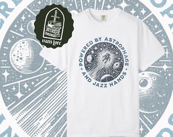 May include: A white short-sleeve t-shirt featuring a circular blue graphic of an astronaut floating in space among planets and stars. The text reads, "POWERED BY ASTROPHAGE AND JAZZ HANDS." A dark green logo with a sword and books reads, "van's Lore."