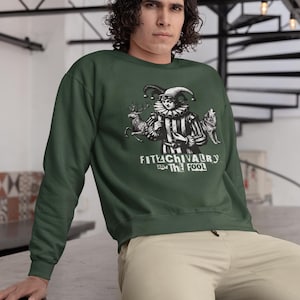 May include: Dark green sweatshirt featuring a black and white illustration of a jester with a deer and wolf. The text "FITACHIVALRY and THE FOOL" is below the illustration. The sweatshirt is a solid color.