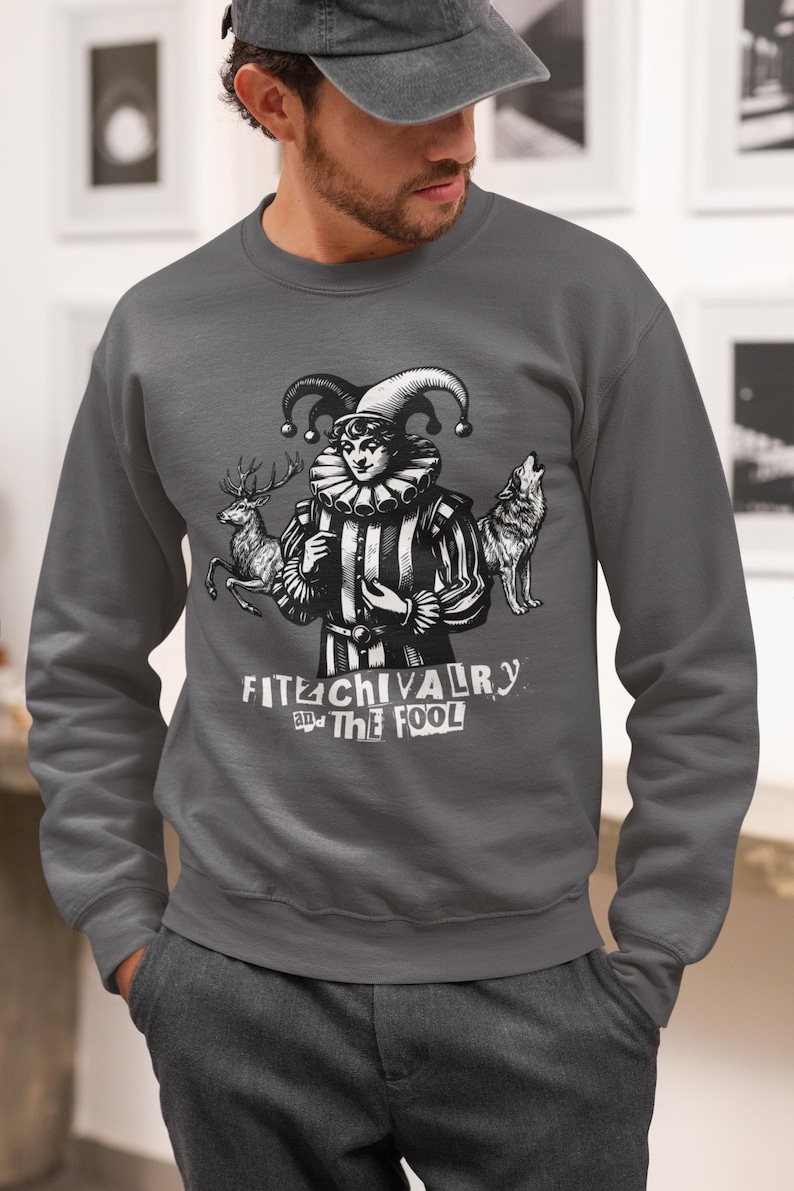 May include: Dark gray sweatshirt featuring a black and white illustration of a jester with a deer and a wolf. The text "FITE CHIVALRY and THE FOOL" is printed below the illustration. The sweatshirt is a crew neck style.